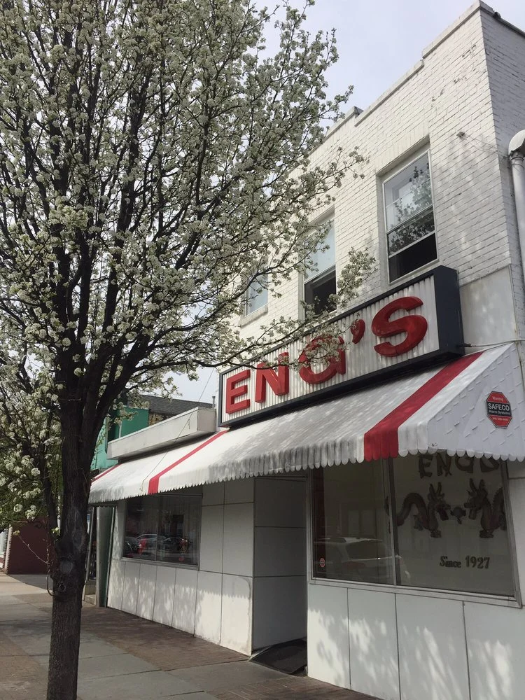 The Broadway storefront of Eng’s with its red sign and striped awning, a flowering tree in front.